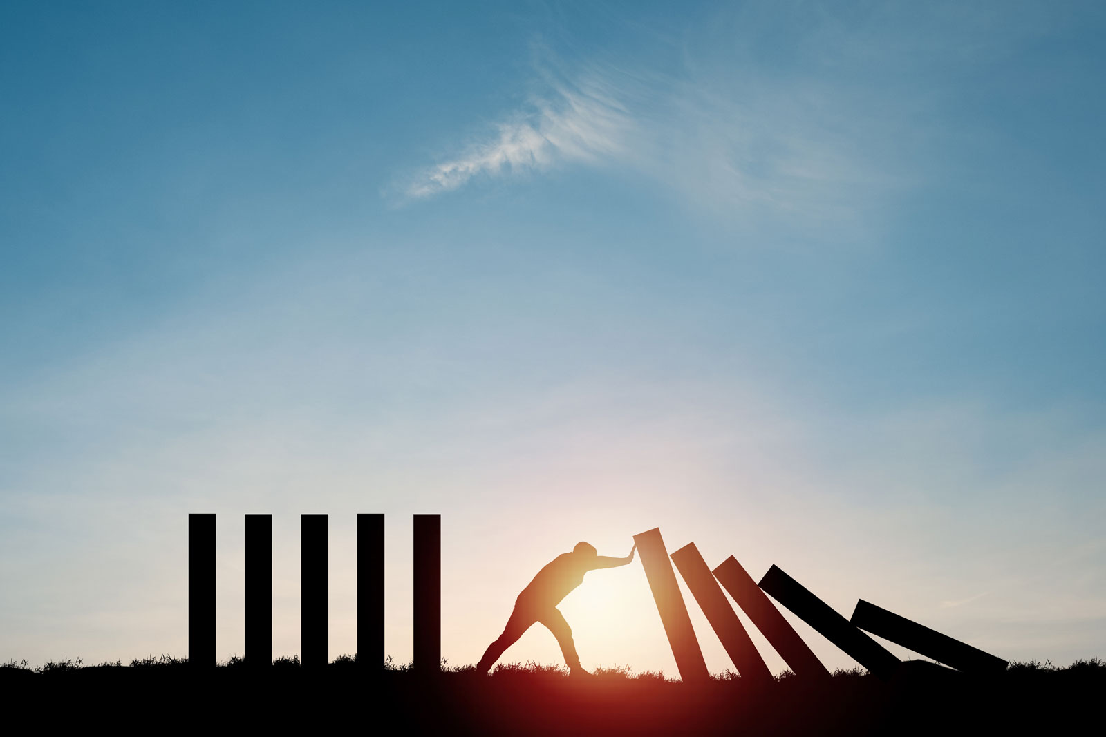 person pushing back giant dominos against a sunset