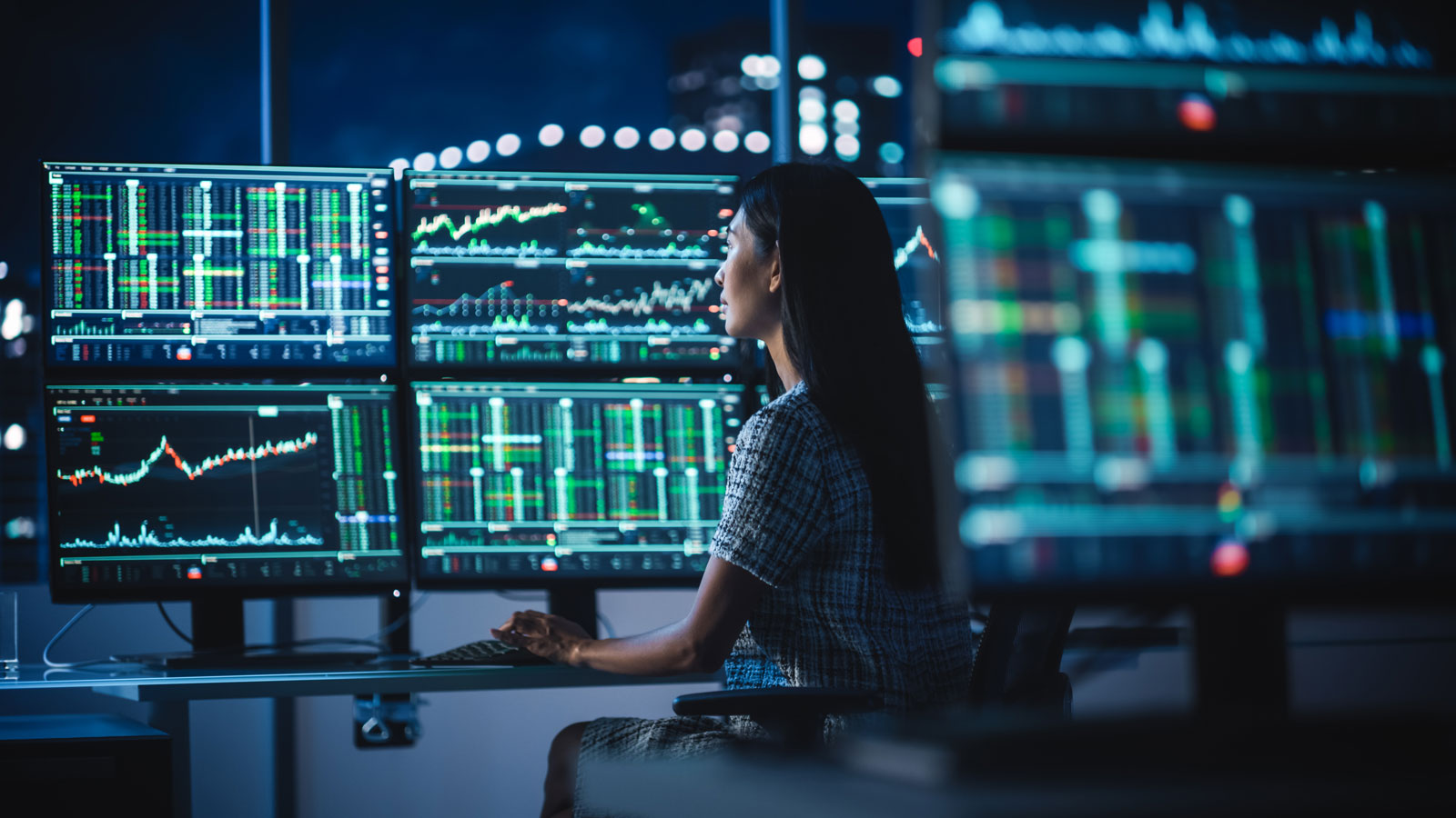 lady sitting in front of a lot of screens in a dark room